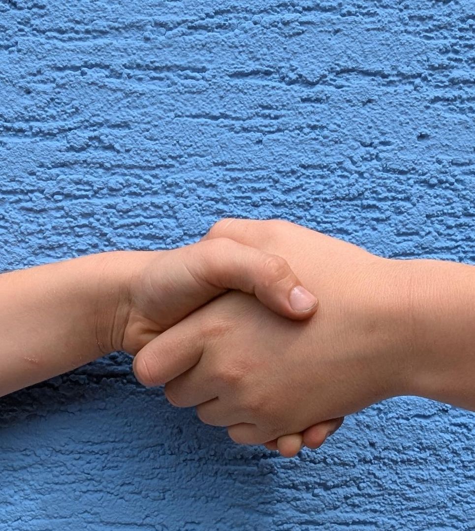 Zwei Hände geben sich vor blauer Wand einen freundlichen Händedruck.